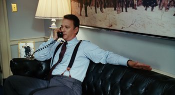 Movie still from “Charlie Wilson's War” (2007), directed by Mike Nichols – A man sitting on a couch talking on the phone; Medium shot, Low angle
