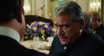 Movie still from “Charlie Wilson's War” (2007), directed by Mike Nichols – An older man sitting in front of a table with flowers; Close Up shot, Over the shoulder angle