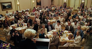 Movie still from “Charlie Wilson's War” (2007), directed by Mike Nichols – A group of people sitting at a table with plates of food; Wide shot, High angle