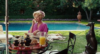 Movie still from “Charlie Wilson's War” (2007), directed by Mike Nichols – A woman sitting at an outdoor table with food and drinks; Wide shot, High angle