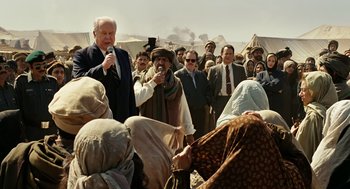 Movie still from “Charlie Wilson's War” (2007), directed by Mike Nichols – A group of people gathered around a man speaking into a microphone; Medium shot, Over the shoulder angle