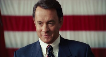 Movie still from “Charlie Wilson's War” (2007), directed by Mike Nichols – A man wearing a suit and tie in front of an american flag; Close Up shot, Low angle
