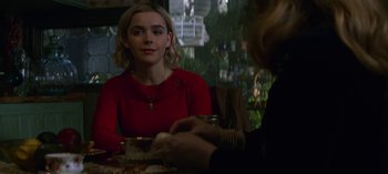 Movie still from “Chilling Adventures of Sabrina” (2018), created by Roberto Aguirre-Sacasa – A woman sitting at a table in front of a plate of food; Medium shot, Over the shoulder angle