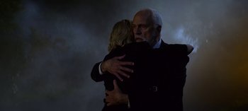 Movie still from “Chilling Adventures of Sabrina” (2018), created by Roberto Aguirre-Sacasa – An older man hugging a younger woman in front of a dark background; Medium shot, Low angle