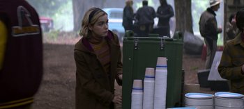 Movie still from “Chilling Adventures of Sabrina” (2018), created by Roberto Aguirre-Sacasa – A woman standing in front of stacks of cups; Medium shot, Over the shoulder angle