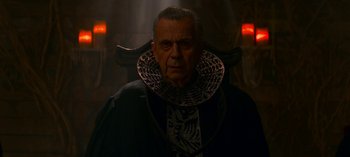 Movie still from “Chilling Adventures of Sabrina” (2018), created by Roberto Aguirre-Sacasa – An older man wearing a black jacket and a neck piece; Medium shot, Low angle
