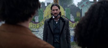 Movie still from “Chilling Adventures of Sabrina” (2018), created by Roberto Aguirre-Sacasa – A man in a suit and tie standing in front of a wall; Medium shot, Over the shoulder angle