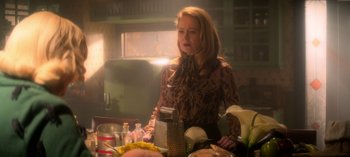 Movie still from “Chilling Adventures of Sabrina” (2018), created by Roberto Aguirre-Sacasa – A woman standing in front of a table with food on top of it; Medium shot, Low angle