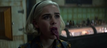 Movie still from “Chilling Adventures of Sabrina” (2018), created by Roberto Aguirre-Sacasa – A woman with blonde hair is licking her tongue; Close Up shot, Over the shoulder angle