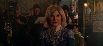 Movie still from “Chilling Adventures of Sabrina” (2018), created by Roberto Aguirre-Sacasa – An older woman wearing a blue dress and pearls in front of a group of people; Close Up shot, Over the shoulder angle