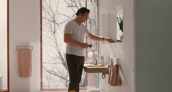 Movie still from “Chloe” (2009), directed by Atom Egoyan – A man in a white t - shirt is in a bathroom; Medium shot, Low angle