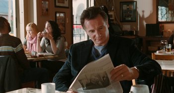 Movie still from “Chloe” (2009), directed by Atom Egoyan – A man sitting at a table reading a newspaper; Medium shot, Over the shoulder angle