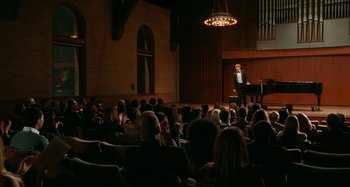 Movie still from “Chloe” (2009), directed by Atom Egoyan – A man is speaking at an event in front of an audience; Extreme Wide shot, High angle
