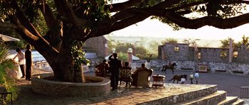 Movie still from “Clear and Present Danger” (1994), directed by Phillip Noyce – A group of people sitting on a patio under a large tree; Extreme Wide shot, Low angle