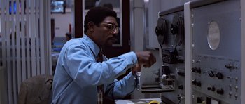 Movie still from “Clear and Present Danger” (1994), directed by Phillip Noyce – A man in a blue dress shirt and red tie is working on a machine; Medium shot, Low angle