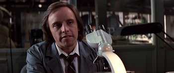 Movie still from “Clear and Present Danger” (1994), directed by Phillip Noyce – A man in a suit and tie holding a microscope; Close Up shot, Over the shoulder angle