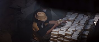 Movie still from “Clear and Present Danger” (1994), directed by Phillip Noyce – A man in a hat is holding a loaf of bread in front of a pile of bread; Medium shot, Overhead angle