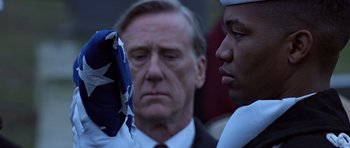 Movie still from “Clear and Present Danger” (1994), directed by Phillip Noyce – A man in a suit and tie holding an american flag next to another man in a suit; Close Up shot, Over the shoulder angle