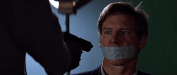Movie still from “Clear and Present Danger” (1994), directed by Phillip Noyce – A man with duct tape over his mouth holding a gun; Close Up shot, Over the shoulder angle