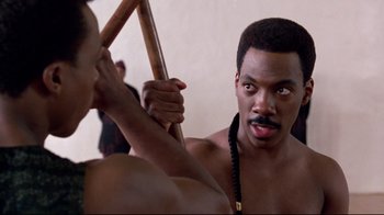 Movie still from “Coming to America” (1988), directed by John Landis – A man holding a stick in front of another man; Close Up shot, Over the shoulder angle