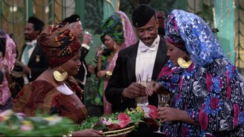 Movie still from “Coming to America” (1988), directed by John Landis – A group of people standing around each other at an event; Medium shot, Over the shoulder angle