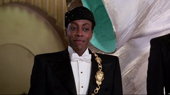 Movie still from “Coming to America” (1988), directed by John Landis – A man in a black suit with a gold chain around his neck; Close Up shot, Low angle