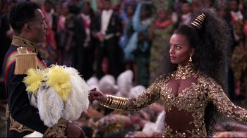 Movie still from “Coming to America” (1988), directed by John Landis – A woman in a gold dress holding a feather fan; Medium shot, Over the shoulder angle
