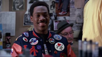Movie still from “Coming to America” (1988), directed by John Landis – A man with a bunch of buttons on his jacket; Close Up shot, Over the shoulder angle