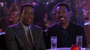 Movie still from “Coming to America” (1988), directed by John Landis – A couple of men sitting next to each other at a table; Medium shot, High angle