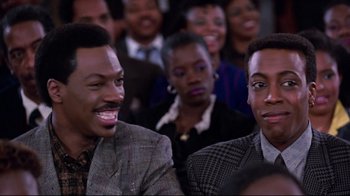 Movie still from “Coming to America” (1988), directed by John Landis – A couple of men sitting next to each other in front of a crowd; Close Up shot, Over the shoulder angle