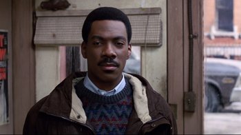 Movie still from “Coming to America” (1988), directed by John Landis – A man in a brown jacket is looking at the camera; Close Up shot, Over the shoulder angle
