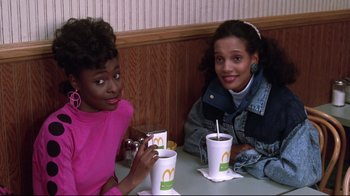 Movie still from “Coming to America” (1988), directed by John Landis – Two young women sitting at a table with drinks; Medium shot, High angle