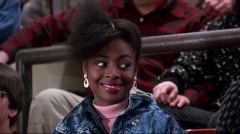 Movie still from “Coming to America” (1988), directed by John Landis – A young woman with a big hair bun sitting in front of other people; Close Up shot, High angle