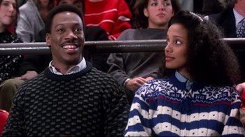 Movie still from “Coming to America” (1988), directed by John Landis – A man and a woman sitting next to each other in front of other people; Medium shot, Low angle