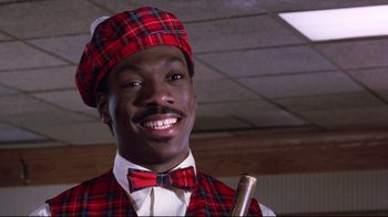 Movie still from “Coming to America” (1988), directed by John Landis – A man wearing a plaid vest , bow tie , and hat holding a cane; Close Up shot, Low angle