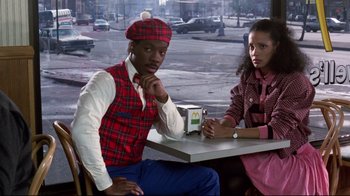 Movie still from “Coming to America” (1988), directed by John Landis – A man and a woman sitting at a table in a restaurant; Medium shot, High angle