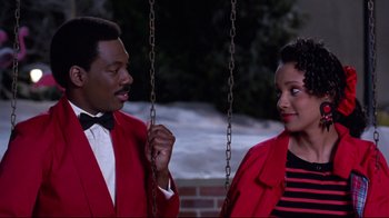 Movie still from “Coming to America” (1988), directed by John Landis – A man and a woman standing next to each other on a swing; Medium shot, Over the shoulder angle