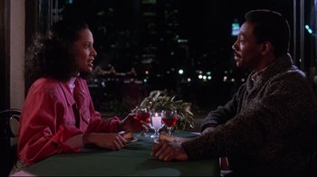 Movie still from “Coming to America” (1988), directed by John Landis – A man and a woman sitting at a table with a glass of wine; Medium shot, Over the shoulder angle
