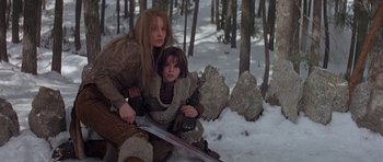 Movie still from “Conan the Barbarian” (1982), directed by John Milius – A woman and a child are sitting in the snow with a sword; Medium shot, Low angle