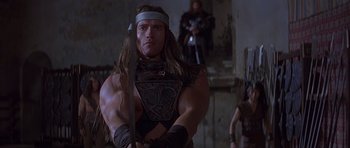 Movie still from “Conan the Barbarian” (1982), directed by John Milius – A person holding a sword in a room; Medium shot, Low angle