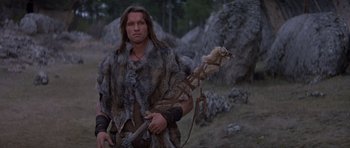 Movie still from “Conan the Barbarian” (1982), directed by John Milius – A man dressed in a fur coat holding an arrow in a field; Medium shot, Low angle
