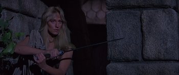 Movie still from “Conan the Barbarian” (1982), directed by John Milius – A woman holding a sword in front of a stone wall; Medium shot, Over the shoulder angle