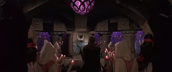 Movie still from “Conan the Barbarian” (1982), directed by John Milius – A group of people sitting in a room holding candles; Wide shot, High angle