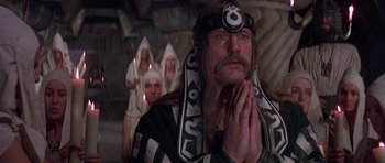 Movie still from “Conan the Barbarian” (1982), directed by John Milius – A group of people standing next to each other in a room; Medium shot, Low angle