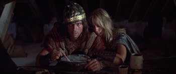 Movie still from “Conan the Barbarian” (1982), directed by John Milius – A man and a woman sitting next to each other on a table; Close Up shot, High angle
