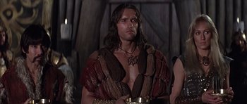Movie still from “Conan the Barbarian” (1982), directed by John Milius – A person wearing a costume and holding a bowl; Medium shot, Low angle
