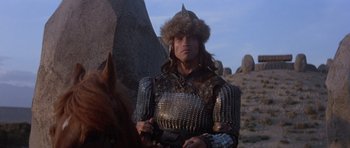 Movie still from “Conan the Barbarian” (1982), directed by John Milius – A man wearing a helmet and armor on a horse in the desert; Medium shot, Low angle