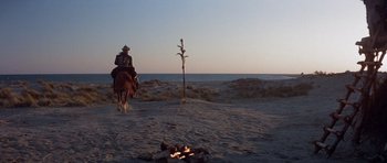 Movie still from “Conan the Barbarian” (1982), directed by John Milius – A man riding a horse in the desert near a bonfire; Extreme Wide shot, Low angle