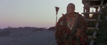 Movie still from “Conan the Barbarian” (1982), directed by John Milius – A man in a native american outfit standing in the desert; Medium shot, Low angle
