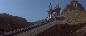 Movie still from “Conan the Barbarian” (1982), directed by John Milius – A group of people standing on top of a bridge; Extreme Wide shot, High angle